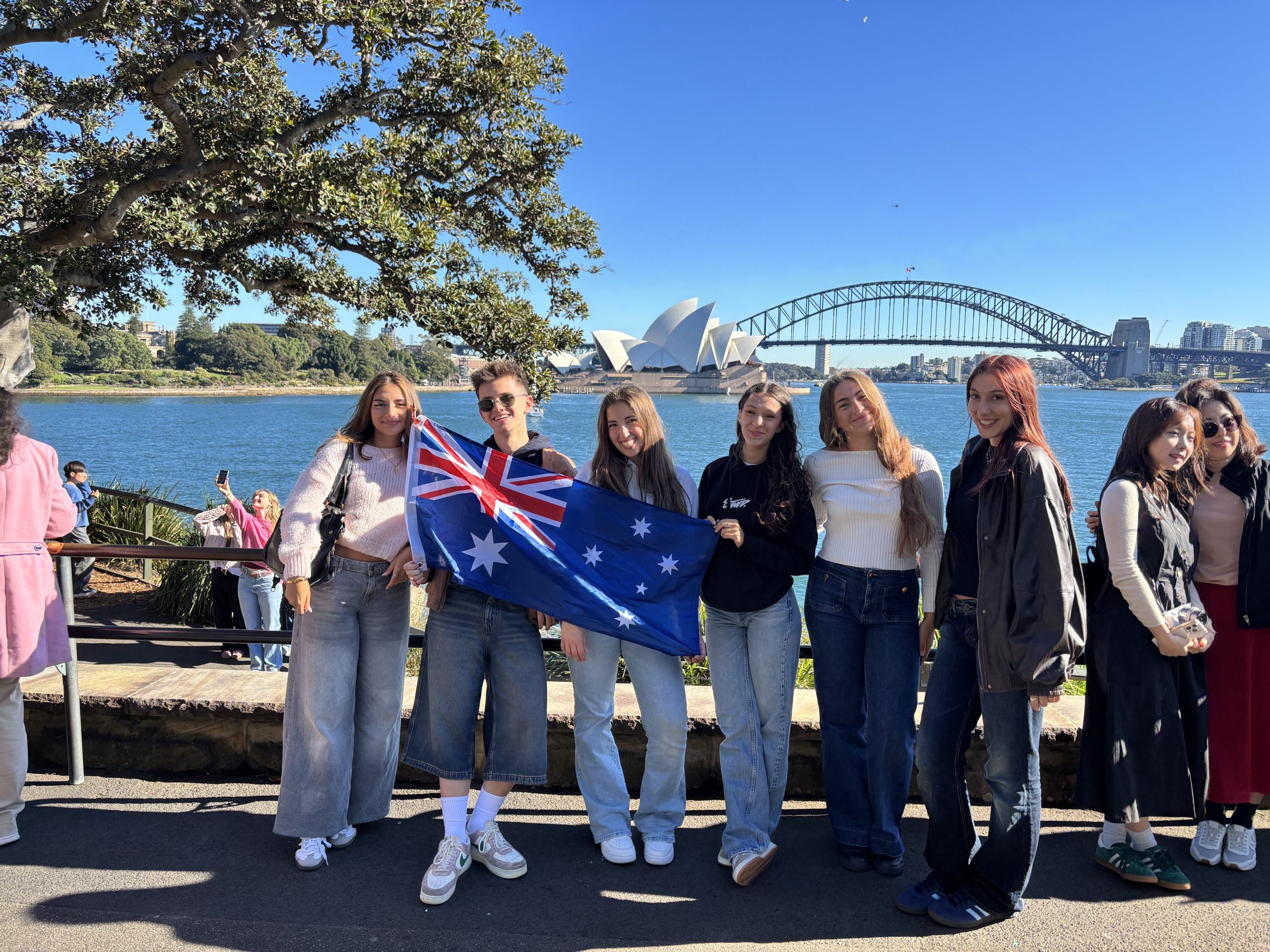 Studenti Destinazione Lingue a Sydney con la bandiera australiana, davanti all’Opera House e all’Harbour Bridge.
